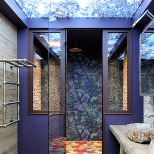 Cette photo montre une douche en alcôve principale éclectique avec un placard sans porte, des portes de placard en bois brun, un mur multicolore, une vasque, un plan de toilette en bois et une cabine de douche à porte battante.