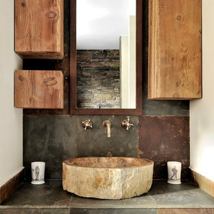 Cette image montre une salle de bain principale chalet de taille moyenne avec un placard à porte plane, des portes de placard en bois vieilli, un carrelage gris, un mur blanc, une vasque et un carrelage de pierre.