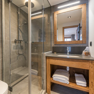 Cette image montre une salle d'eau chalet de taille moyenne avec un placard sans porte, des portes de placard en bois brun, une douche d'angle, un WC suspendu, un carrelage gris, un mur blanc, un lavabo encastré, un sol gris, une cabine de douche à porte battante, un plan de toilette gris, meuble simple vasque et meuble-lavabo encastré.