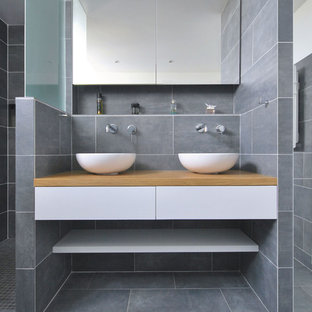 Idée de décoration pour une grand salle d'eau design avec un placard sans porte, des portes de placard blanches, une douche à l'italienne, un carrelage gris, une vasque, un plan de toilette en bois, aucune cabine et un plan de toilette marron.