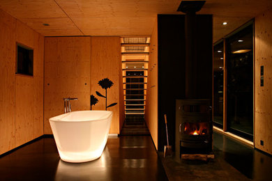 Réalisation d'une grande salle de bain principale design en bois brun avec une baignoire indépendante et un sol noir.