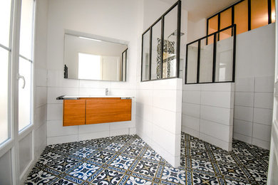 Cette image montre une grande salle d'eau urbaine avec une douche ouverte, WC suspendus, un carrelage blanc, des carreaux en terre cuite, un mur blanc, carreaux de ciment au sol, un plan vasque, un plan de toilette en surface solide, un sol noir et un plan de toilette blanc.