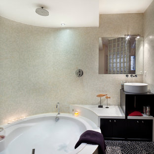 Réalisation d'une salle de bain principale design de taille moyenne avec une vasque, des portes de placard noires, un combiné douche/baignoire, un carrelage beige, carrelage en mosaïque, un mur beige, un sol en galet et un bain bouillonnant.