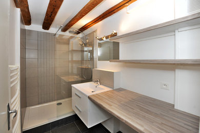 Réalisation d'une salle de bain principale minimaliste avec une douche ouverte, un carrelage beige, un mur blanc, un sol en ardoise, un lavabo suspendu et un plan de toilette en bois.