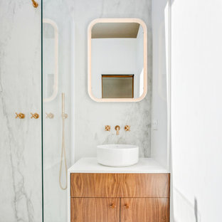 Réalisation d'une salle d'eau design avec un placard à porte plane, des portes de placard en bois brun, un carrelage blanc, des dalles de pierre, un mur blanc, une vasque et un plan de toilette blanc.