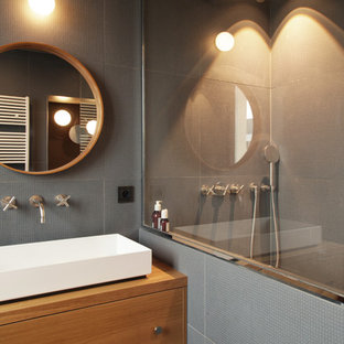 Cette image montre une petit salle de bain design avec des portes de placard en bois brun, un carrelage gris, des carreaux de céramique, un mur gris, une grande vasque, un plan de toilette en bois, aucune cabine et un plan de toilette marron.