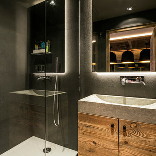 Cette image montre une salle d'eau design avec des portes de placard en bois brun, une douche d'angle, un placard à porte plane, un carrelage gris, un mur gris et une grande vasque.