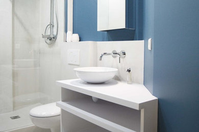 Cette image montre une salle d'eau design de taille moyenne avec WC suspendus, un mur bleu, sol en béton ciré, une vasque, un plan de toilette en béton, un placard sans porte, des portes de placard blanches, une douche d'angle et un carrelage blanc.