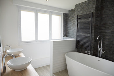 Cette image montre une salle de bain principale minimaliste de taille moyenne avec une baignoire indépendante, un carrelage gris, un carrelage de pierre, un mur blanc, parquet clair, un lavabo suspendu, un plan de toilette en bois, une douche ouverte et WC suspendus.