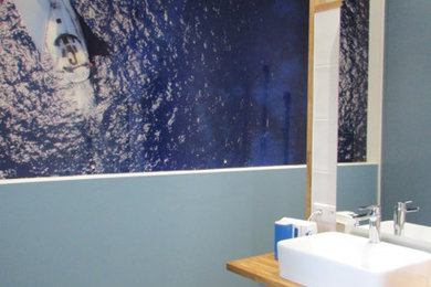 Ejemplo de cuarto de baño marinero con ducha a ras de suelo, sanitario de pared, baldosas y/o azulejos blancos, paredes azules, lavabo tipo consola y encimera de madera