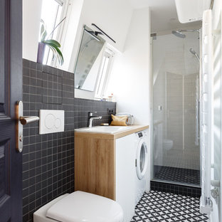Cette image montre une petit douche en alcôve design avec un placard à porte plane, des portes de placard blanches, un WC suspendu, un carrelage noir, un carrelage blanc, un mur blanc, un lavabo posé, un plan de toilette en bois, un sol multicolore, une cabine de douche à porte battante, un plan de toilette marron, des carreaux de céramique et un sol en carreaux de ciment.