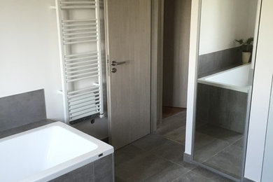 Aménagement d'une grande salle de bain contemporaine avec un placard à porte affleurante, des portes de placard grises, une baignoire encastrée, une douche à l'italienne, un carrelage gris, des carreaux de céramique, un mur gris et un sol en carrelage de céramique.