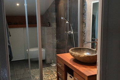 Bild på ett mellanstort vintage en-suite badrum, med luckor med profilerade fronter, vita skåp, en kantlös dusch, en vägghängd toalettstol, grå kakel, keramikplattor, grå väggar, klinkergolv i keramik, ett nedsänkt handfat och träbänkskiva