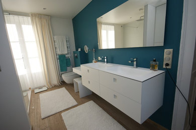 Photo of a large contemporary ensuite bathroom in Nancy with flat-panel cabinets, white cabinets, a walk-in shower, a wall mounted toilet, blue walls, light hardwood flooring, a wall-mounted sink, brown floors, an open shower and white worktops.