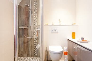 ストラスブールにある高級な小さなトランジショナルスタイルのおしゃれなバスルーム (浴槽なし) (バリアフリー、壁掛け式トイレ、白いタイル、セラミックタイル、マルチカラーの壁、コンソール型シンク、ガラスの洗面台、フラットパネル扉のキャビネット、ベージュのキャビネット、ベージュの床、白い洗面カウンター、セラミックタイルの床) の写真
