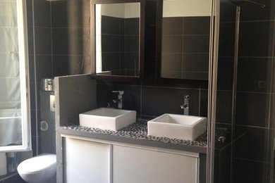 Modelo de cuarto de baño principal actual con puertas de armario blancas, ducha a ras de suelo, sanitario de pared, baldosas y/o azulejos grises, paredes grises y lavabo sobreencimera