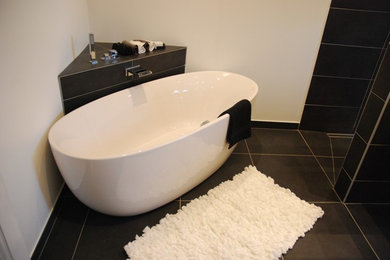 Cette image montre une grande salle de bain principale design avec une baignoire posée, une douche à l'italienne, un carrelage noir, des carreaux de céramique, un mur noir, un sol en carrelage de céramique, une grande vasque, un plan de toilette en surface solide et un sol noir.