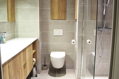 Cette photo montre une salle de bain principale tendance en bois clair de taille moyenne avec un placard à porte affleurante, une douche à l'italienne, WC suspendus, un carrelage gris, des carreaux de céramique, un mur gris, un sol en carrelage de céramique, une grande vasque, un plan de toilette en quartz et un sol gris.