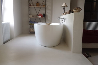 Modelo de cuarto de baño de estilo de casa de campo con ducha a ras de suelo, paredes blancas, suelo de cemento, aseo y ducha y encimera de cemento