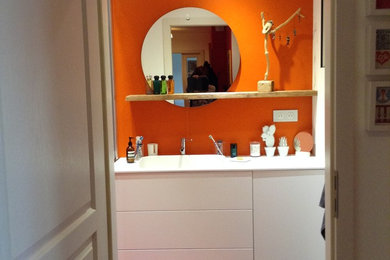 Aménagement d'une petite salle de bain moderne avec des portes de placard blanches, des carreaux de céramique, un mur orange, un sol en carrelage de céramique, un plan de toilette en surface solide et un lavabo intégré.