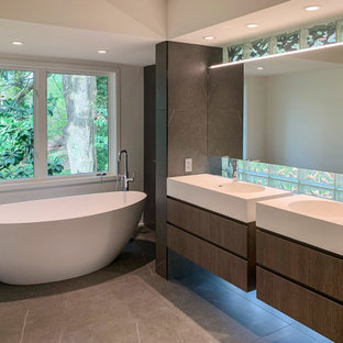Aménagement d'une grand salle de bain principale contemporaine avec un placard à porte plane, des portes de placard en bois brun, une baignoire indépendante, un mur gris, un lavabo intégré, un sol gris, un plan de toilette blanc, meuble double vasque et meuble-lavabo suspendu.