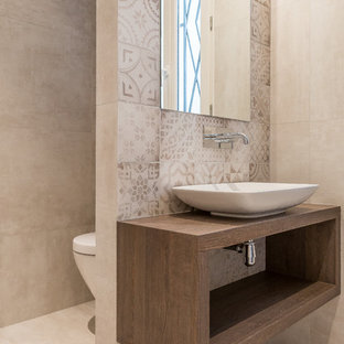 Cette image montre une salle de bain principale et beige et marron design de taille moyenne avec une vasque, un placard sans porte, un plan de toilette en bois, un WC suspendu, un carrelage beige, des carreaux de béton, un mur beige et un plan de toilette marron.