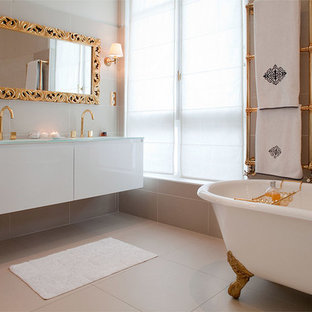 Cette image montre une très grand salle de bain principale traditionnelle avec une baignoire sur pieds, un plan de toilette en verre et un mur beige.