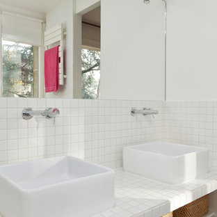 Cette photo montre une salle de bain tendance de taille moyenne avec un mur blanc, un sol en bois foncé, une vasque, un plan de toilette en carrelage, un carrelage blanc, un placard sans porte et des portes de placard blanches.