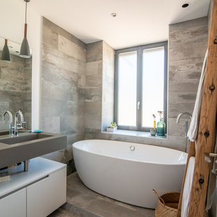 Inspiration pour une salle d'eau design avec un placard à porte plane, des portes de placard blanches, une baignoire indépendante, un carrelage gris, un mur blanc, un lavabo intégré, un sol gris et un plan de toilette gris.