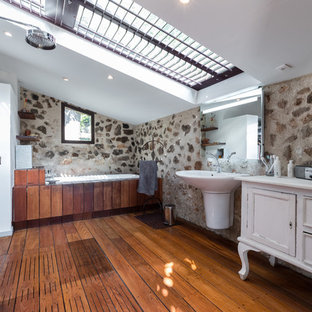 Cette image montre une salle de bain principale méditerranéenne avec un placard en trompe-l'oeil, des portes de placard blanches, un espace douche bain, un sol en bois foncé, un lavabo suspendu, un sol marron et aucune cabine.