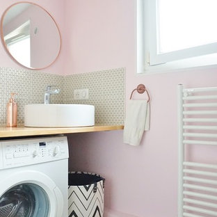 Inspiration pour une salle d'eau design de taille moyenne avec un placard sans porte, un mur rose, un sol en bois clair, une vasque, un plan de toilette en bois et un sol beige.
