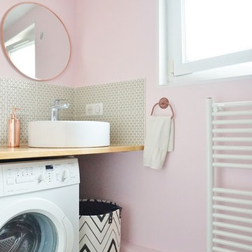 Une petite salle d'eau rose et une petite cuisine grise dans un immeuble ancien