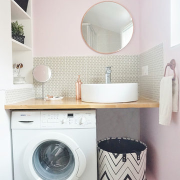 Une petite salle d'eau rose et une petite cuisine grise dans un immeuble ancien