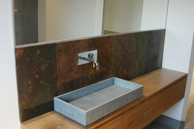 Cette image montre une salle d'eau design avec un carrelage gris, un carrelage de pierre, un mur blanc, sol en béton ciré, un lavabo posé et un plan de toilette en bois.
