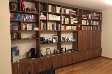 Ejemplo de sala de estar con biblioteca cerrada minimalista de tamaño medio con suelo de madera clara y televisor retractable