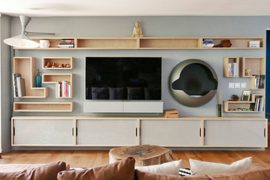 Modelo de sala de estar con biblioteca abierta contemporánea de tamaño medio con paredes grises, suelo de madera en tonos medios, chimeneas suspendidas, marco de chimenea de metal y televisor colgado en la pared
