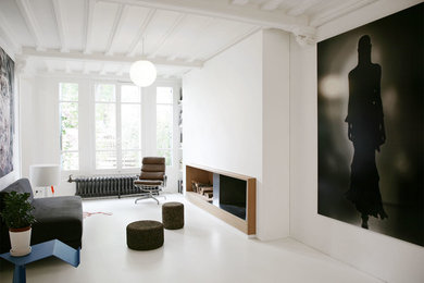 パリにあるコンテンポラリースタイルのおしゃれなファミリールーム (白い壁、標準型暖炉、漆喰の暖炉まわり、白い床、黒いソファ) の写真