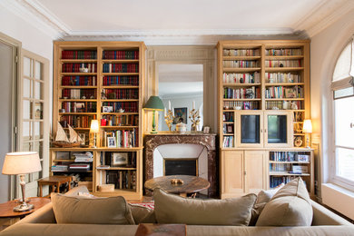 Cette photo montre une salle de séjour chic de taille moyenne et fermée avec une bibliothèque ou un coin lecture, un mur blanc, un sol en bois brun, une cheminée standard, un manteau de cheminée en pierre et un téléviseur dissimulé.