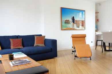 Imagen de sala de estar con biblioteca abierta retro de tamaño medio con paredes blancas, suelo de madera clara y suelo beige