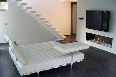 Exemple d'une salle de séjour tendance de taille moyenne et ouverte avec un mur blanc, une cheminée standard, un manteau de cheminée en plâtre et un téléviseur fixé au mur.