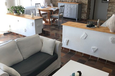 Modelo de sala de estar abierta de estilo de casa de campo grande con paredes blancas, suelo de baldosas de terracota, estufa de leña, televisor independiente y suelo marrón