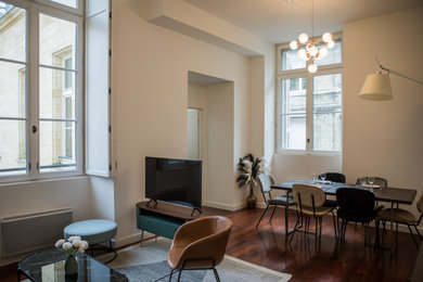 На фото: гостиная комната в стиле неоклассика (современная классика) с белыми стенами, темным паркетным полом и отдельно стоящим телевизором