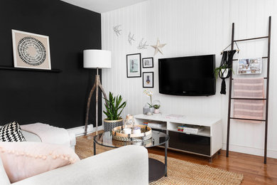 Modelo de sala de estar nórdica pequeña sin chimenea con paredes negras, suelo de madera en tonos medios y televisor colgado en la pared