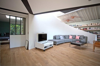 Ejemplo de sala de estar abierta actual extra grande sin chimenea con paredes blancas, suelo de madera clara, suelo beige y televisor retractable