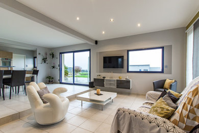 Imagen de sala de estar abierta contemporánea de tamaño medio sin chimenea con paredes grises, suelo de baldosas de cerámica, televisor colgado en la pared y suelo beige