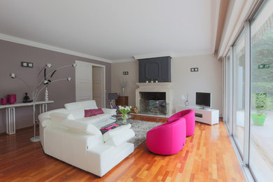 Cette photo montre une grande salle de séjour tendance fermée avec une cheminée standard, un téléviseur indépendant, un mur multicolore et un sol en bois brun.