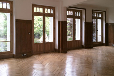 Exemple d'une salle de séjour chic de taille moyenne et fermée avec un mur blanc, parquet clair, une cheminée standard, un manteau de cheminée en pierre, un sol marron et aucun téléviseur.