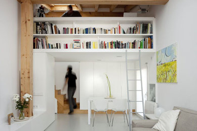 Inspiration pour une salle de séjour mansardée ou avec mezzanine minimaliste de taille moyenne avec un mur blanc, sol en béton ciré, un sol gris, une bibliothèque ou un coin lecture, aucune cheminée et un téléviseur fixé au mur.