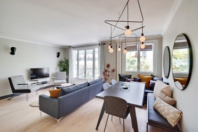 Ejemplo de sala de estar abierta contemporánea de tamaño medio con paredes grises, suelo de madera clara y televisor colgado en la pared