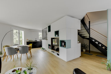 Foto de sala de estar abierta actual de tamaño medio sin chimenea con paredes verdes, suelo de madera clara, pared multimedia y suelo beige